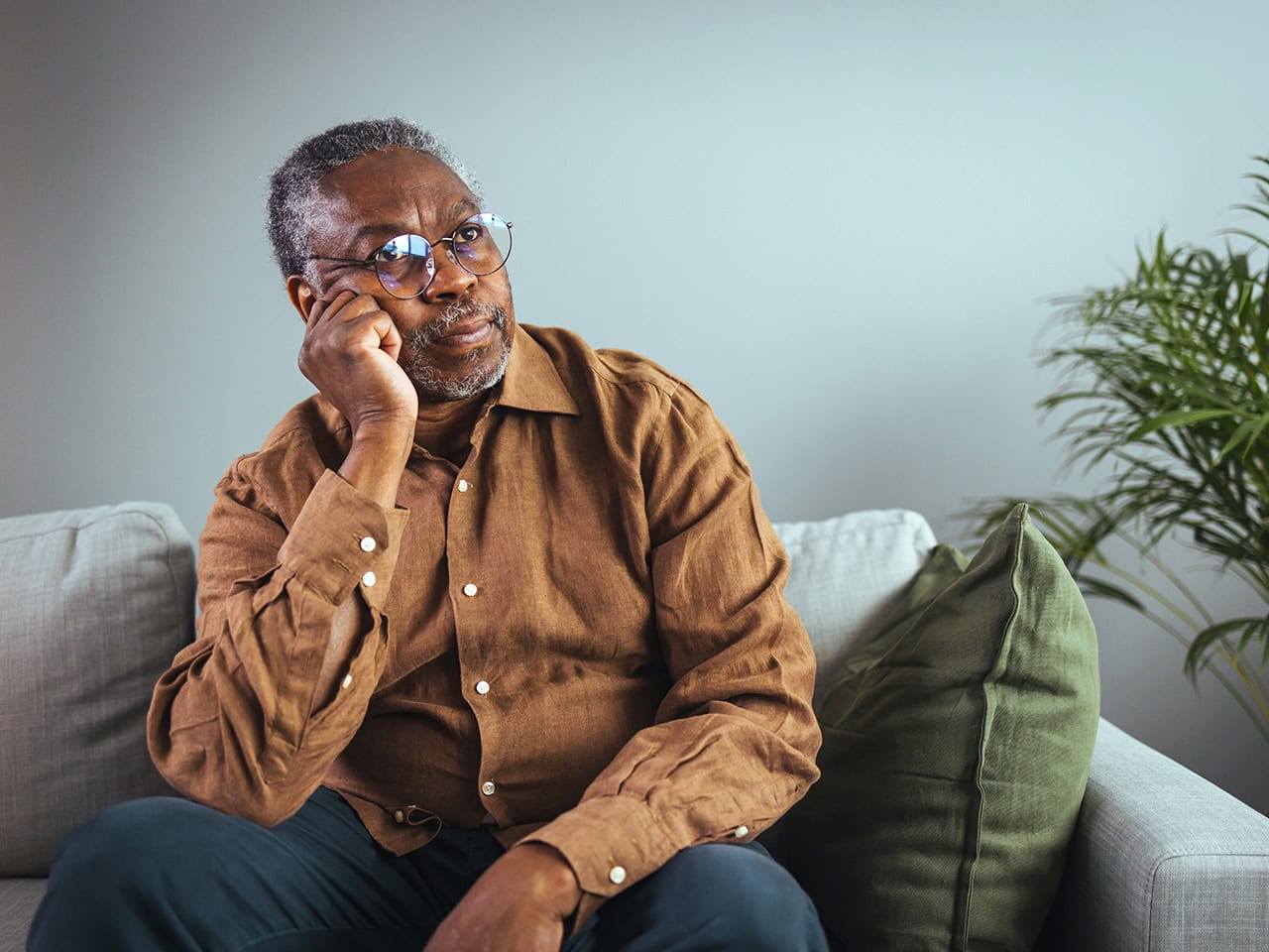 Elderly man with glasses sitting pensively on couch