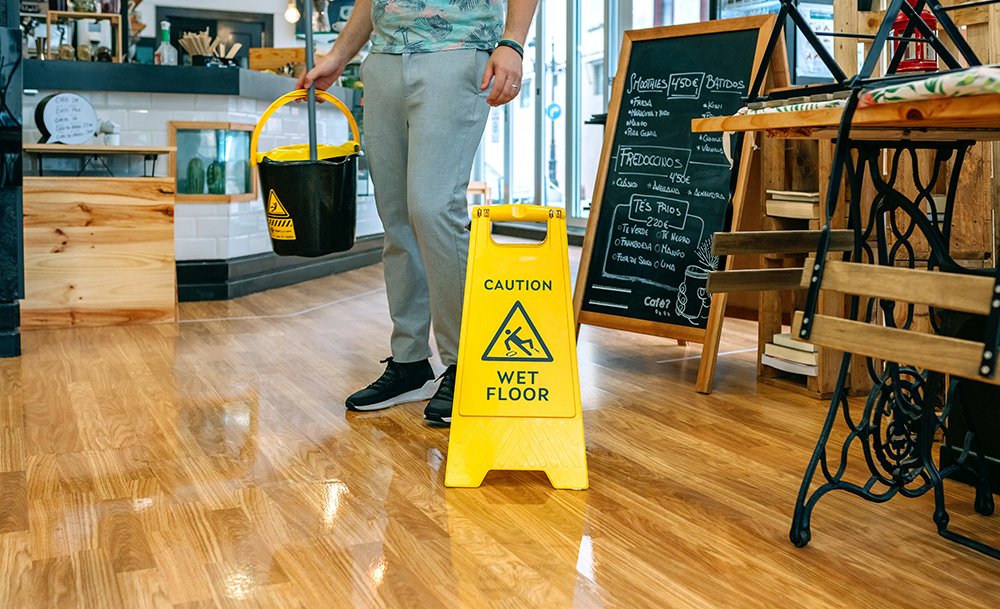 Worker mopping a floor with a wet mop, potentially having a customer slip and fall and in need of personal injury lawyers
